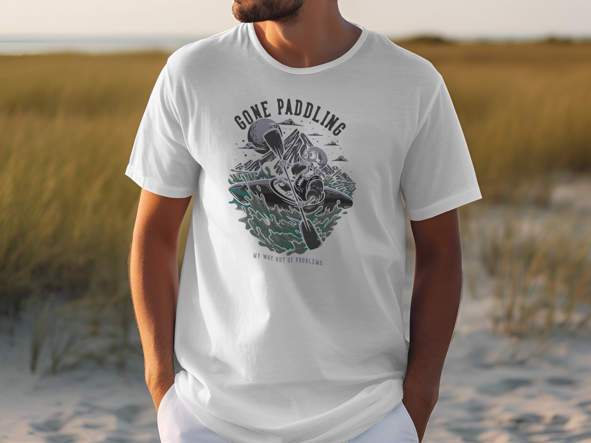 White t-shirt with graphic of skeleton kayaking, text "GONE PADDLING MY WAY OUT OF PROBLEMS".