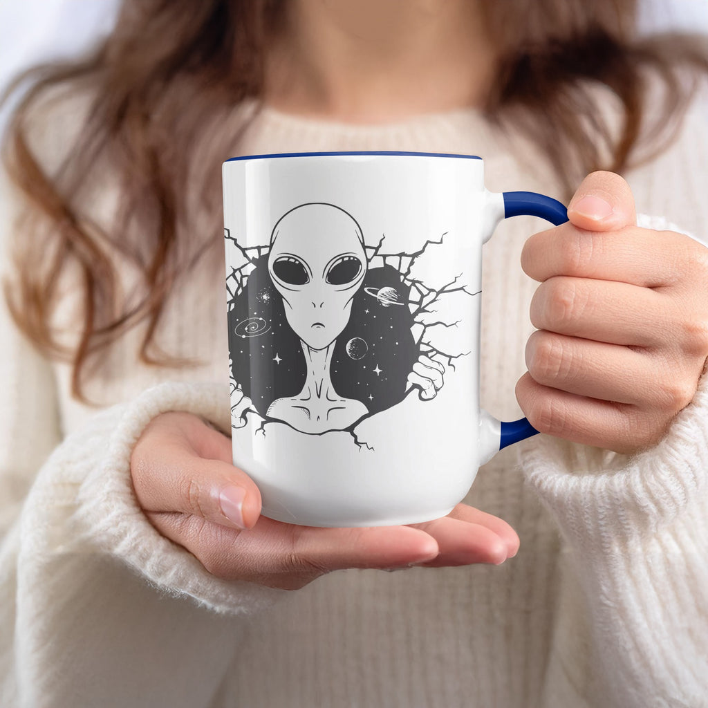 White mug with blue rim featuring an alien face breaking through a starry background.