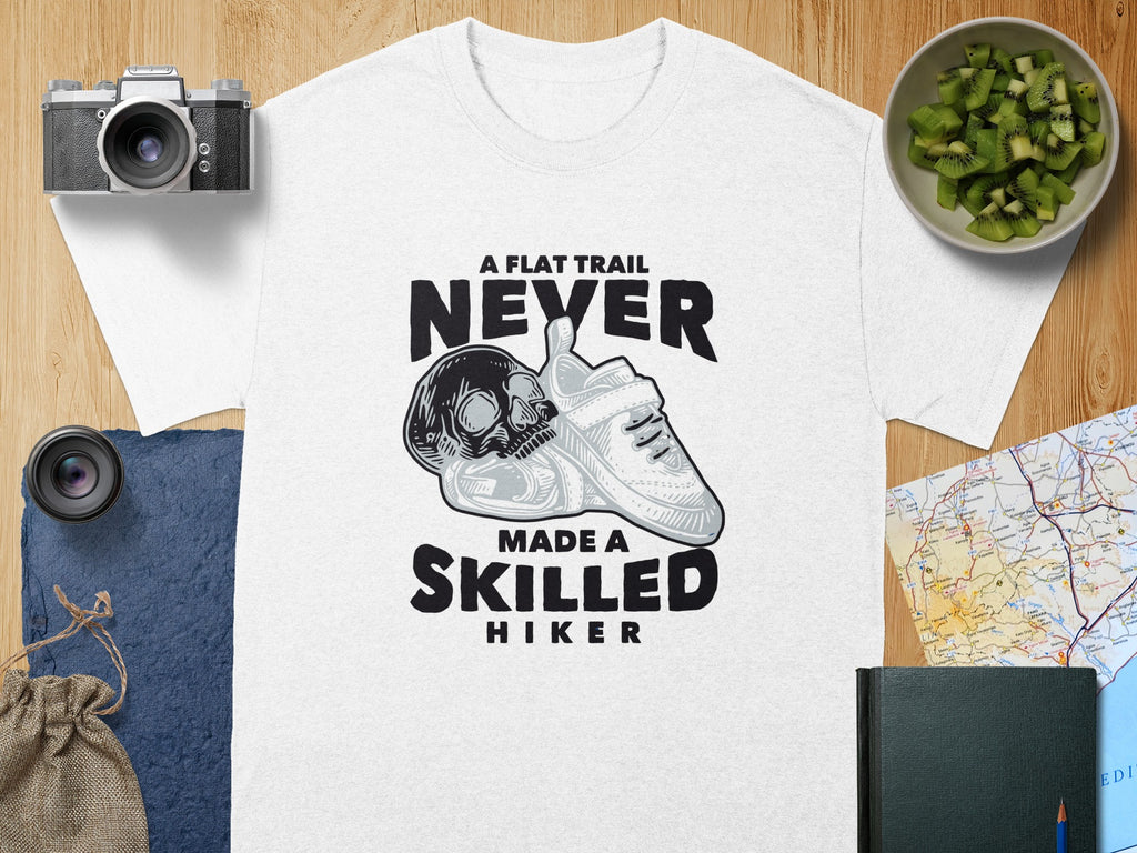 White t-shirt with skull, sneaker, and text "A flat trail never made a skilled hiker".