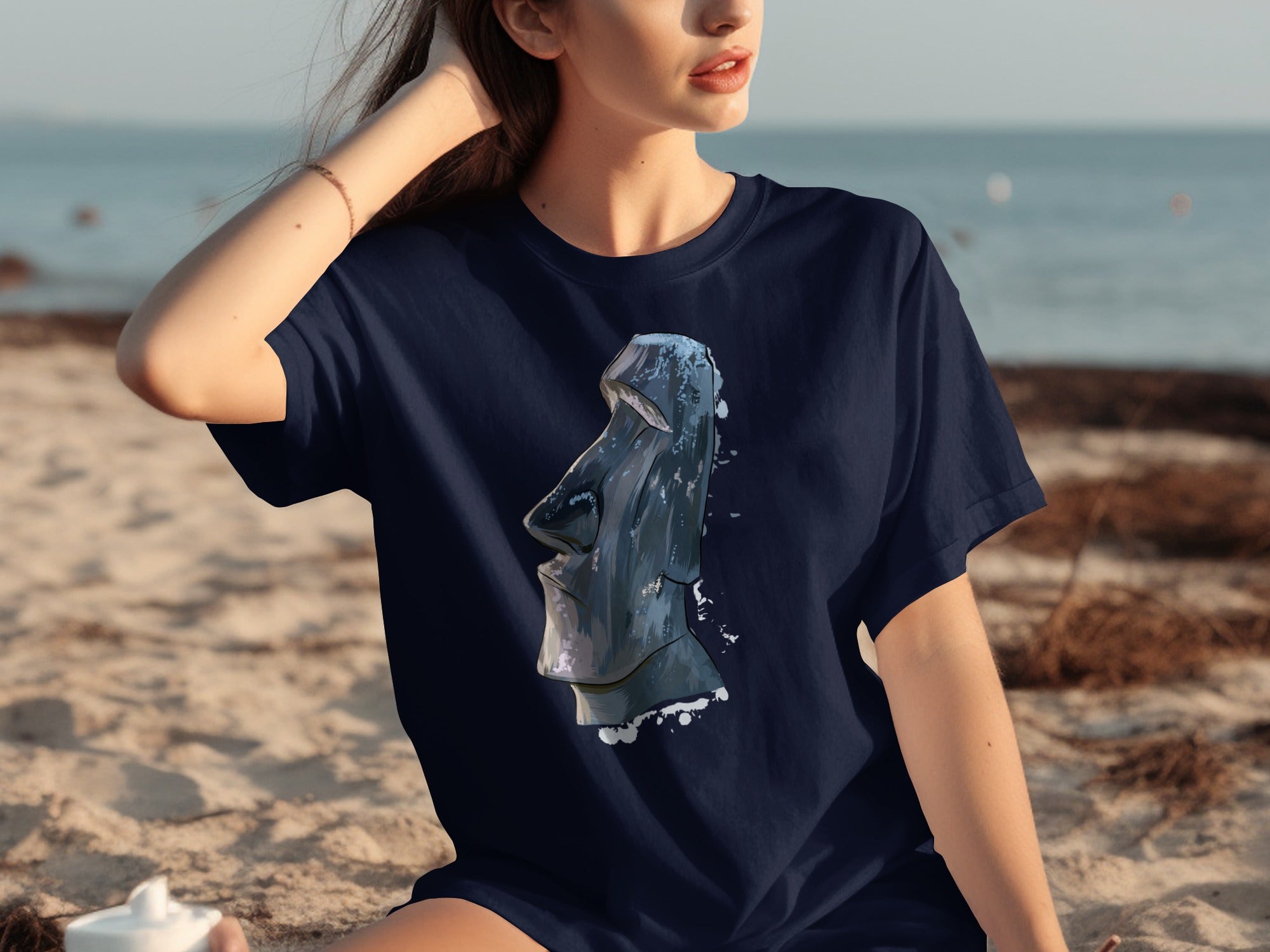 Navy t-shirt with Moai statue graphic on a sandy beach background.