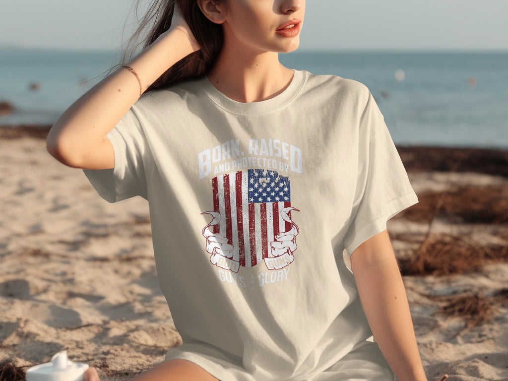 T-shirt with American flag graphic and text: "Born, Raised, and Protected by God, Guns, Guys & Glory".