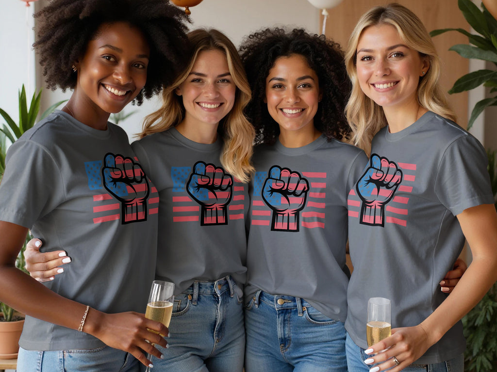 Four smiling women wear grey t-shirts with a raised fist graphic and US flag print.