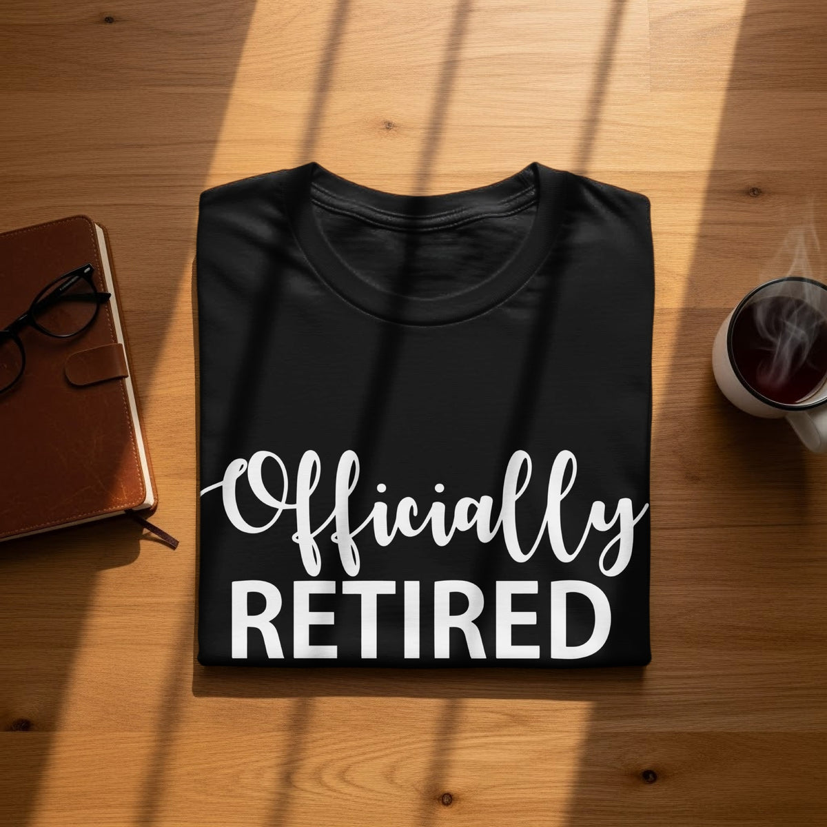 Black t-shirt with white text "Officially RETIRED" displayed on a wooden surface.