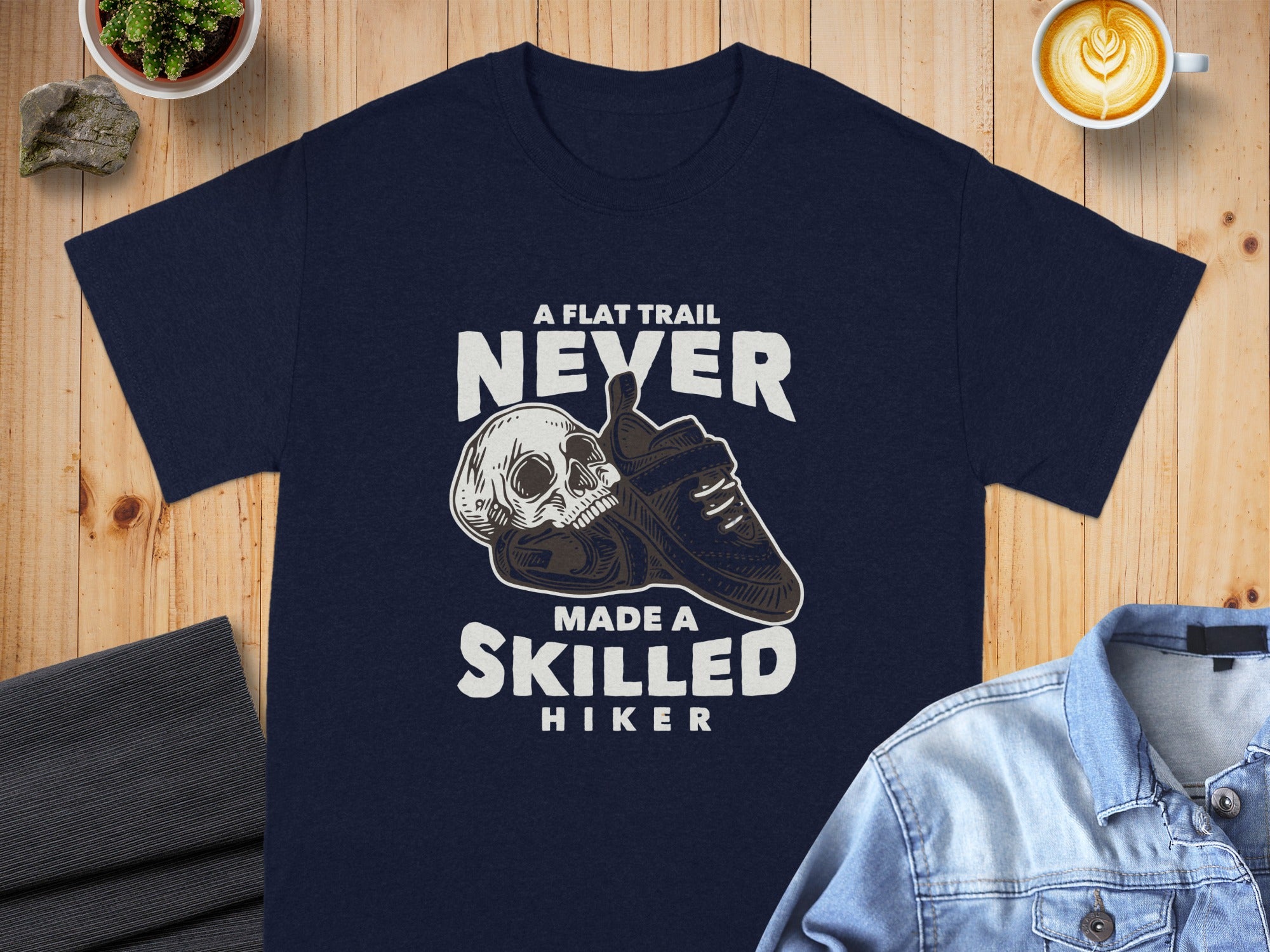 Navy t-shirt with "A flat trail never made a skilled hiker" text and skull graphic.