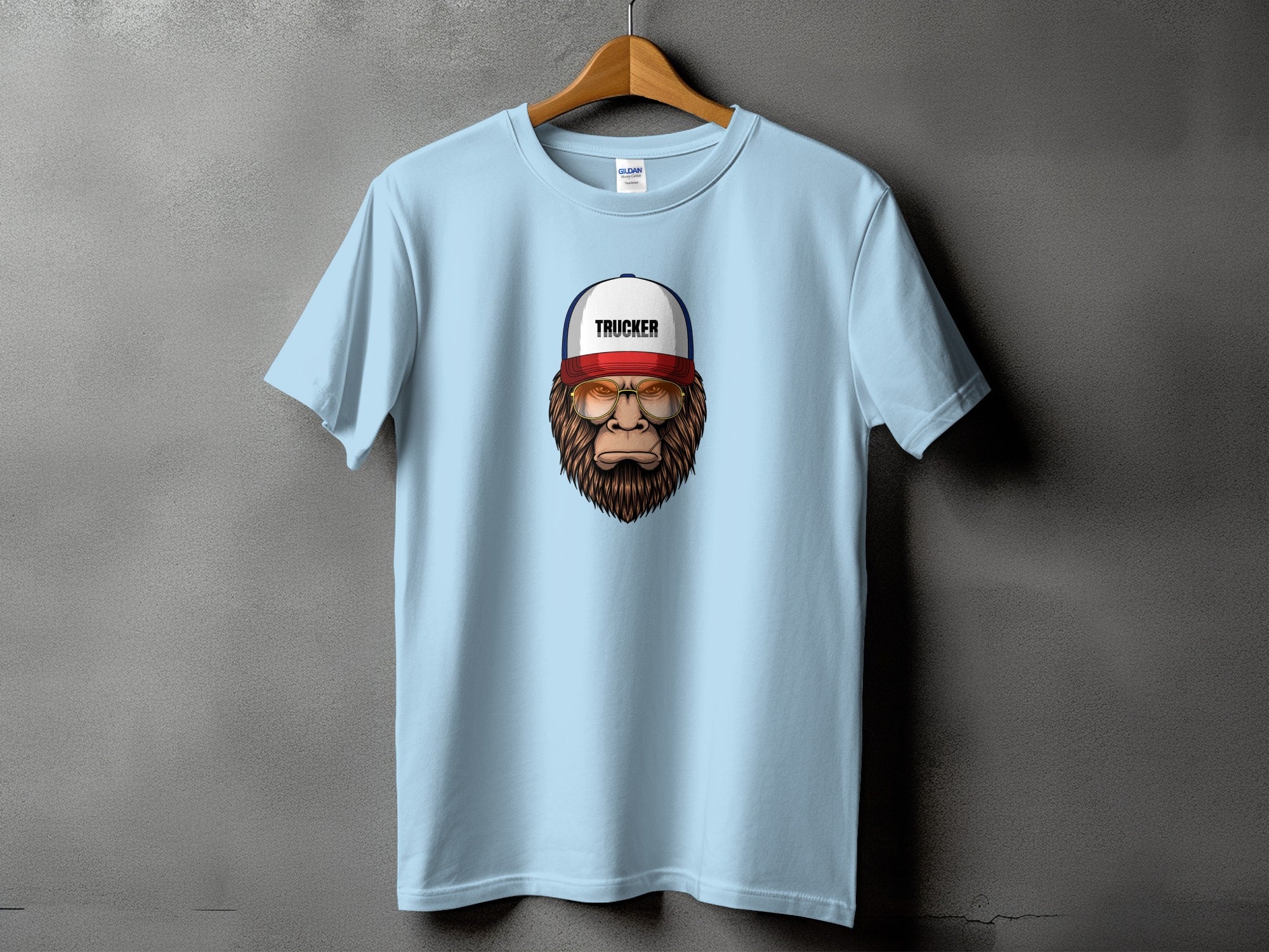 Light blue t-shirt with Big Foot graphic wearing "TRUCKER" hat and sunglasses.