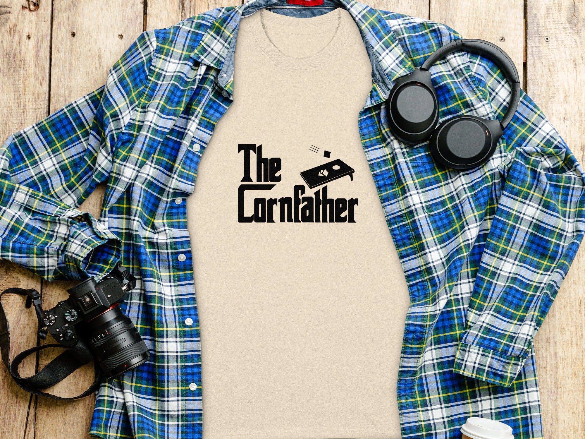 Beige t-shirt with "The Cornfather" text and cornhole graphic, laid flat.