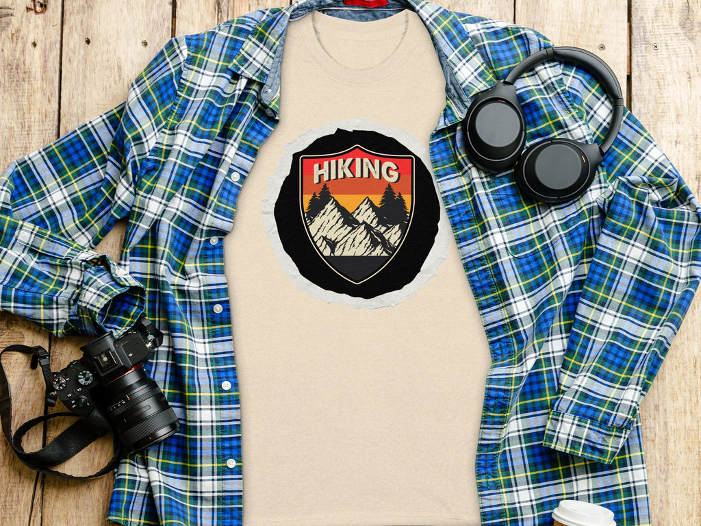 Beige t-shirt with hiking graphic, plaid shirt and headphones, wooden background.