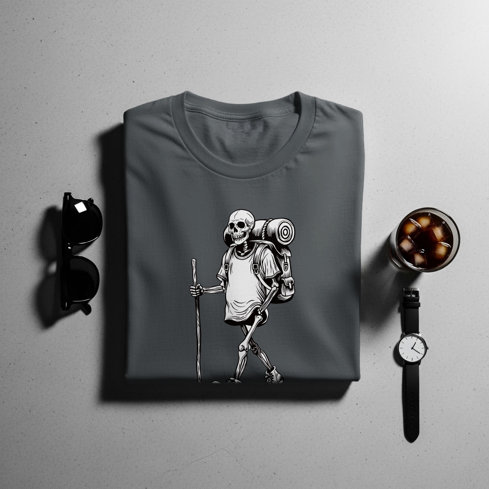 Dark grey t-shirt with skeleton hiker graphic, sunglasses, watch, and iced drink.