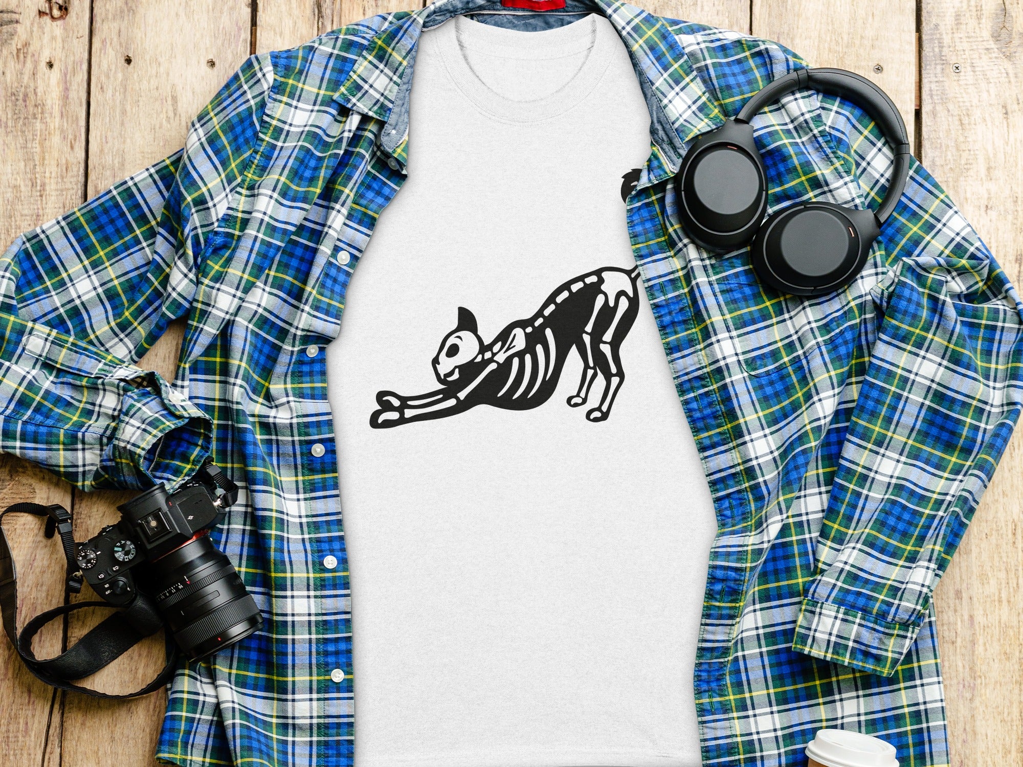 White t-shirt with a black cat skeleton graphic alongside a plaid shirt and headphones.