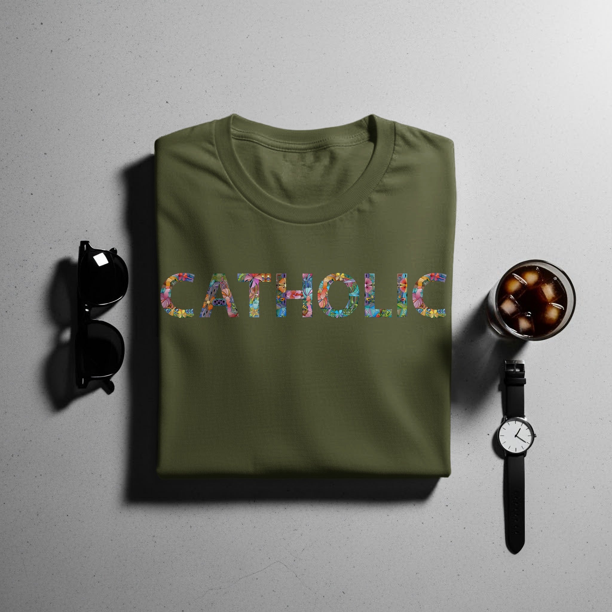 Green t-shirt with colorful "CATHOLIC" text, sunglasses, and a drink.