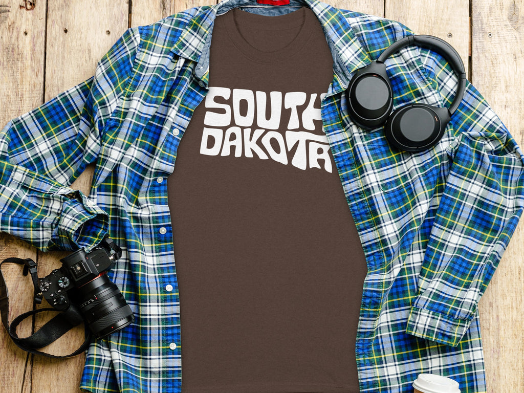 Brown t-shirt with white "SOUTH DAKOTA" text, laid out with a plaid shirt.