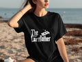 Black t-shirt with white text "The Cornfather" and a cornhole board graphic.