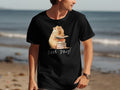 Black t-shirt with graphic of capybara wearing glasses reading book on stack of books.