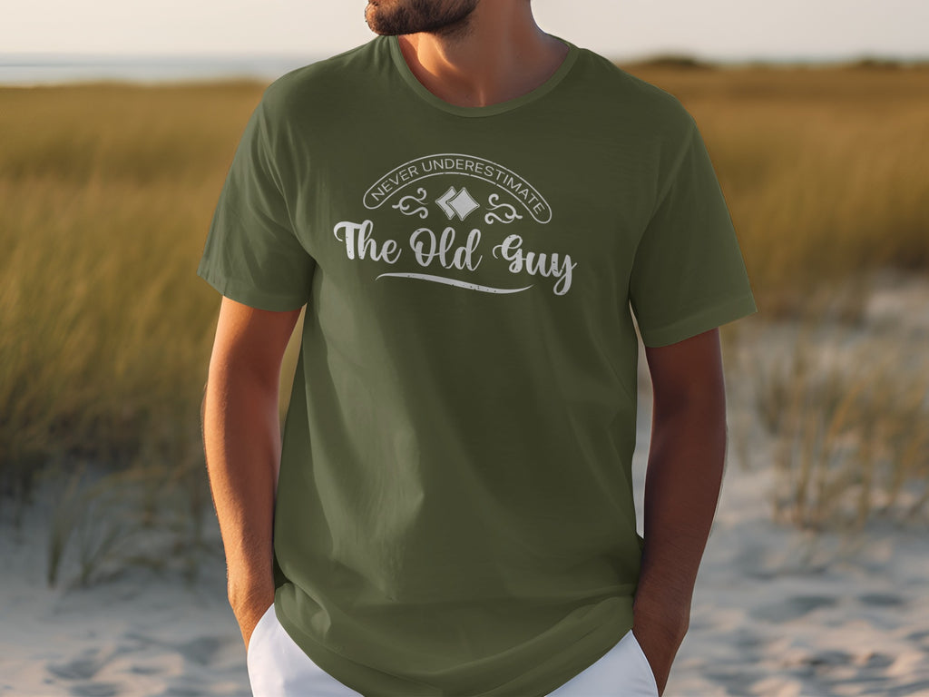 Olive green t-shirt with white text "Never Underestimate The Old Guy".