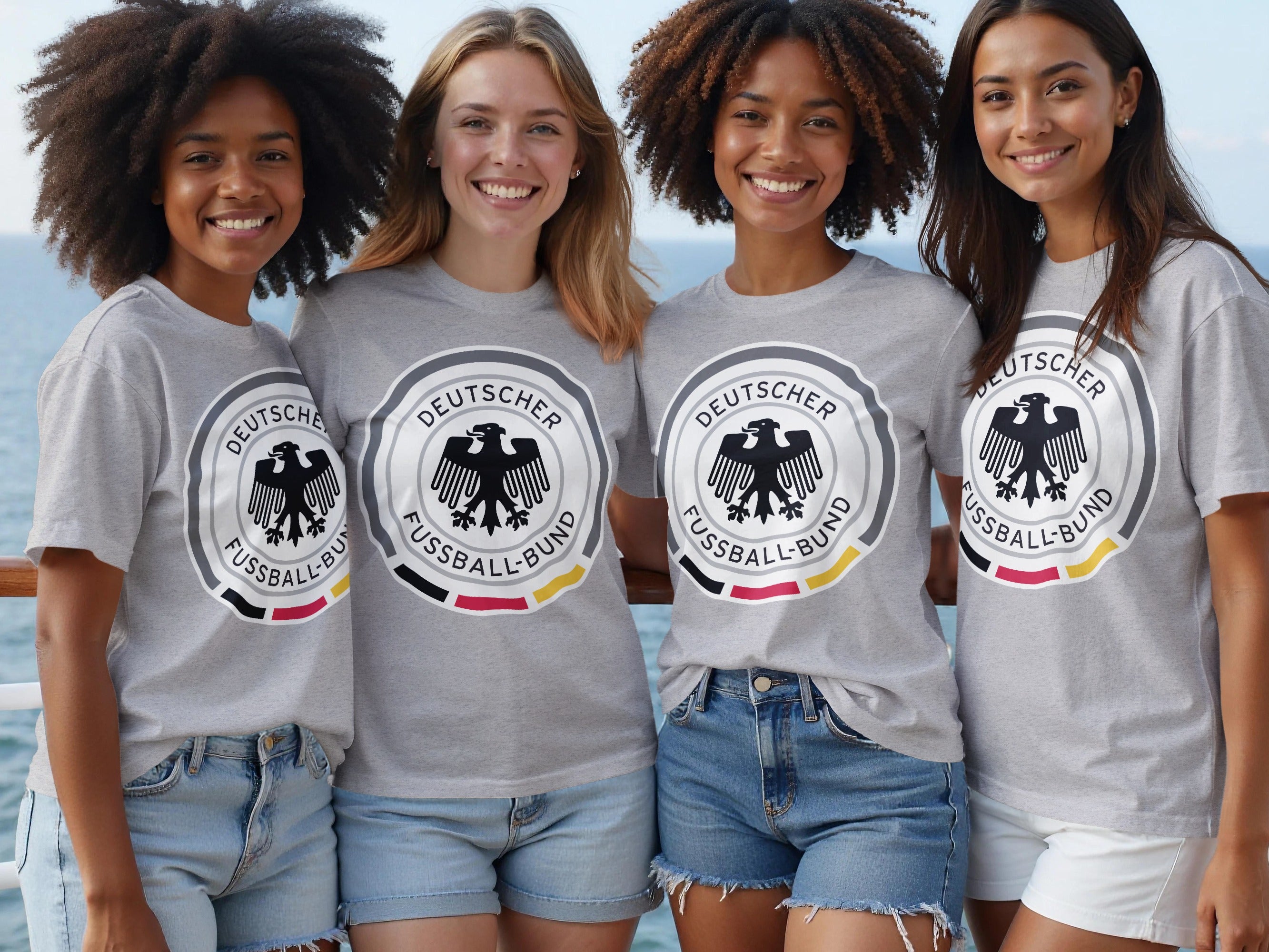 Four smiling women wear grey t-shirts with the German Football Association crest.