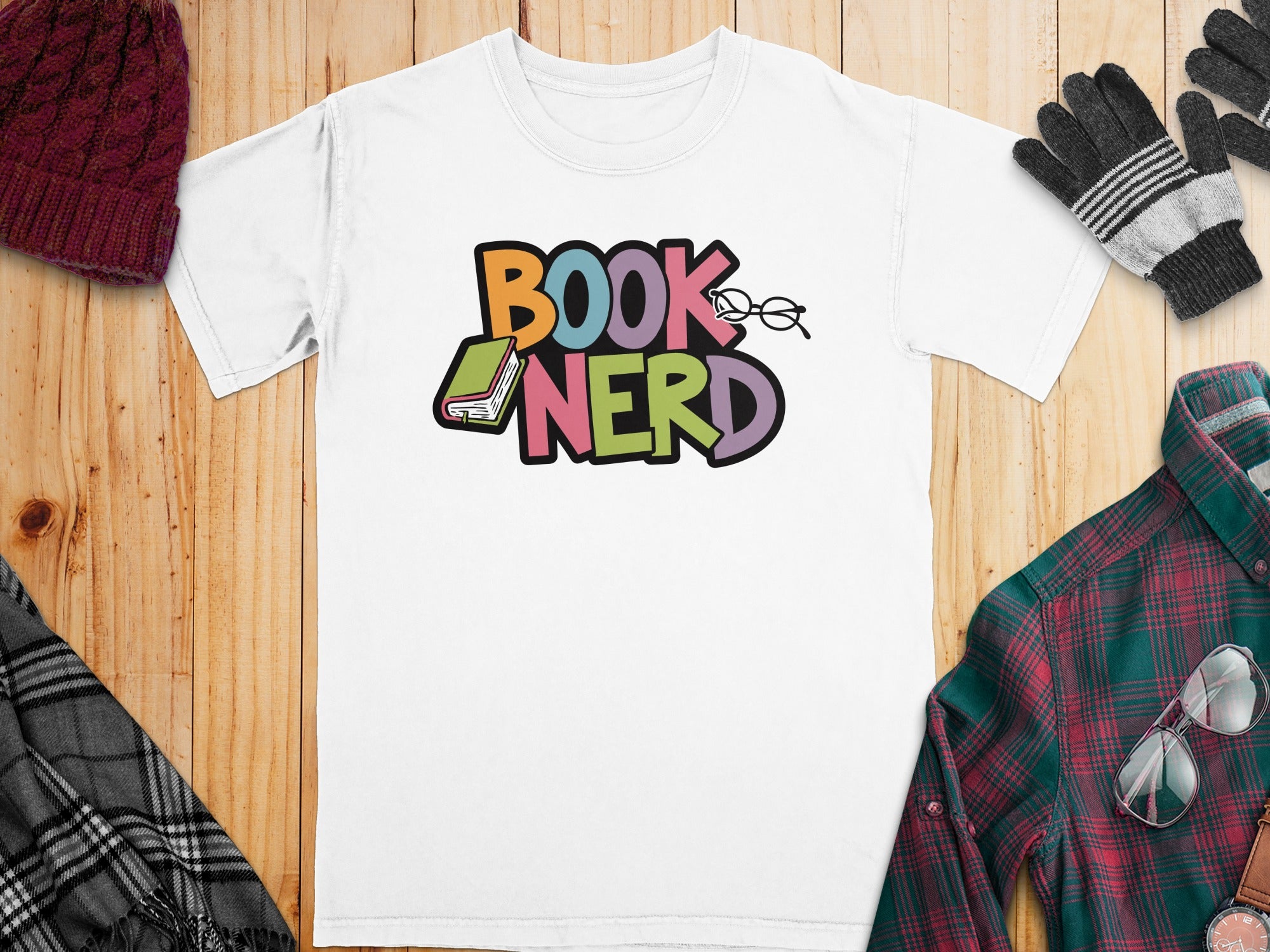White t-shirt with colorful "BOOK NERD" text, a book, and glasses graphic.