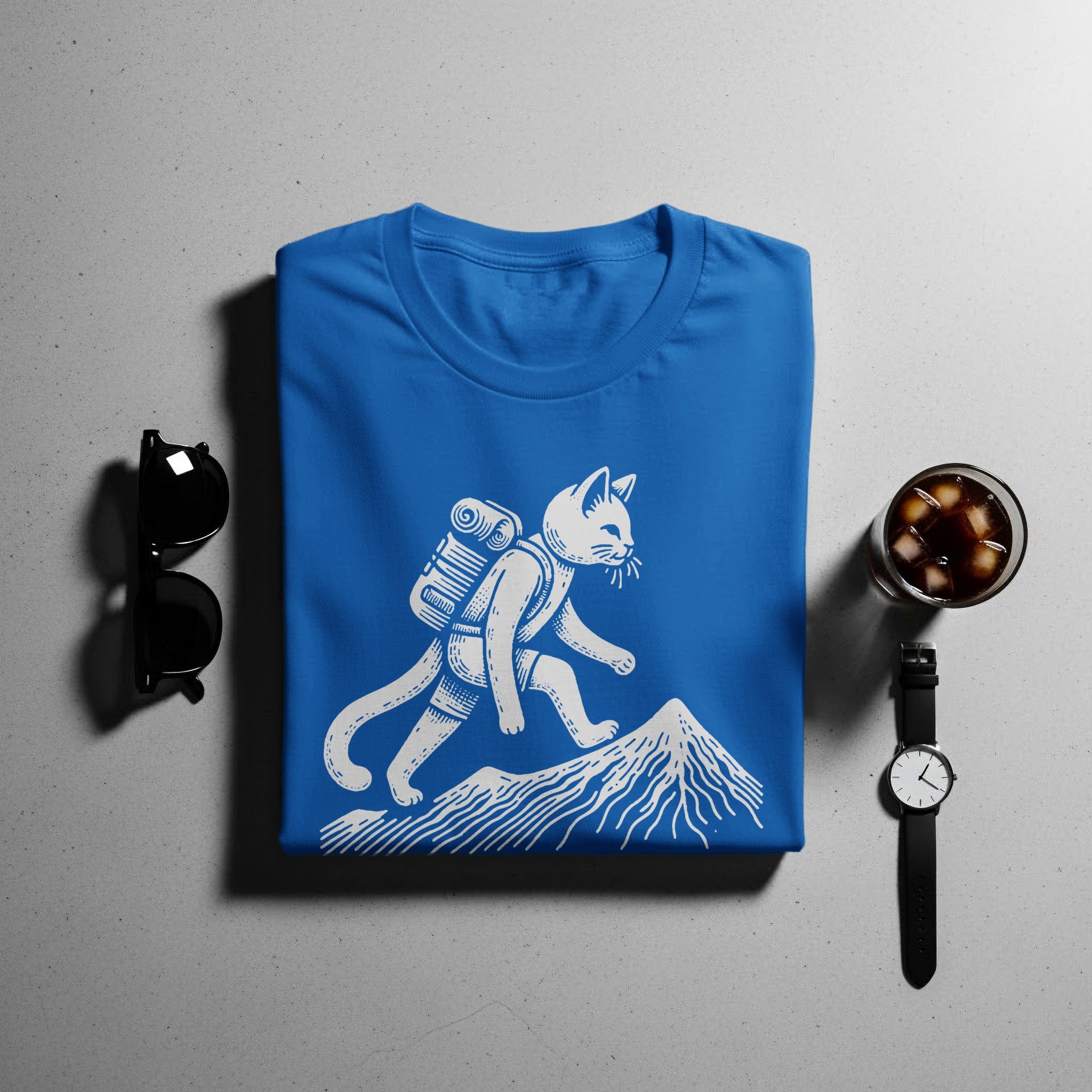 Blue t-shirt with white graphic of a cat hiking a mountain.