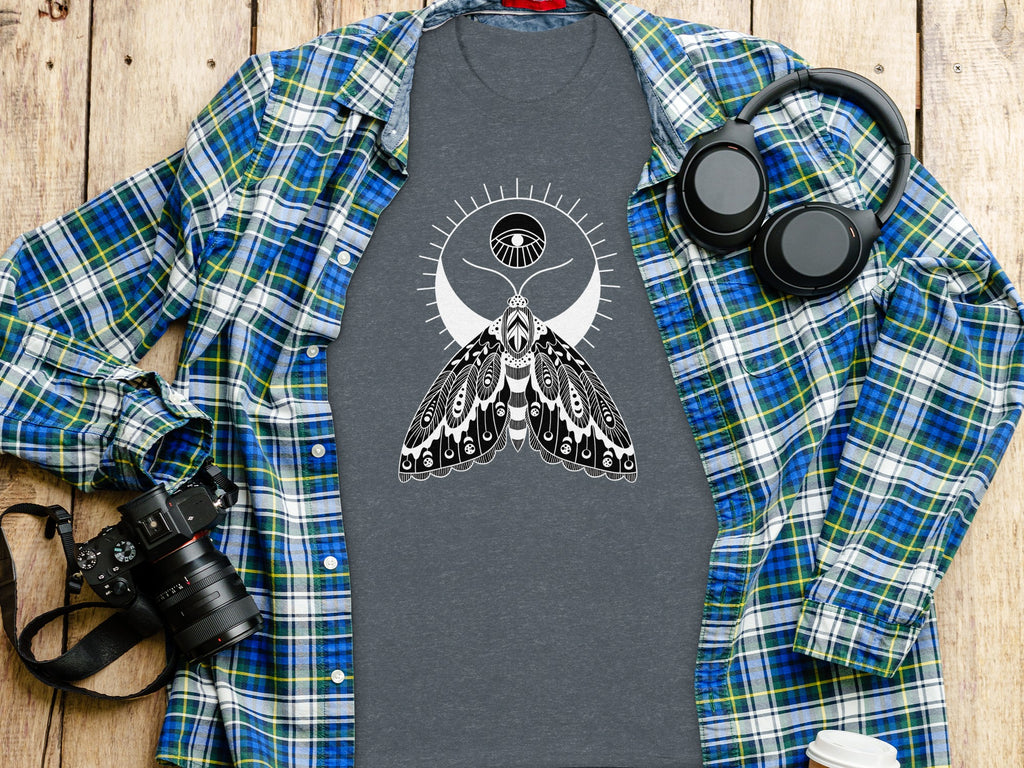 Grey t-shirt with white moth and eye design, open plaid shirt, headphones, and camera.