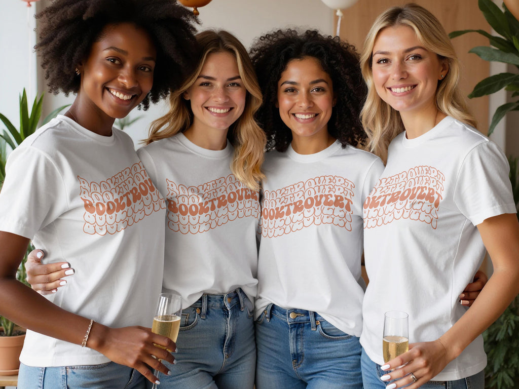Four smiling women wear white t-shirts with "BOOKTROVERT" text in a retro, wavy font.
