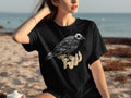Black t-shirt with crow skull design on a hand, worn by a woman on a beach.