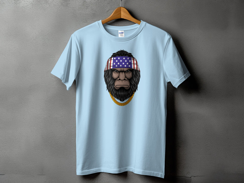 Light blue t-shirt with a Bigfoot graphic wearing an American flag bandana and gold chain.