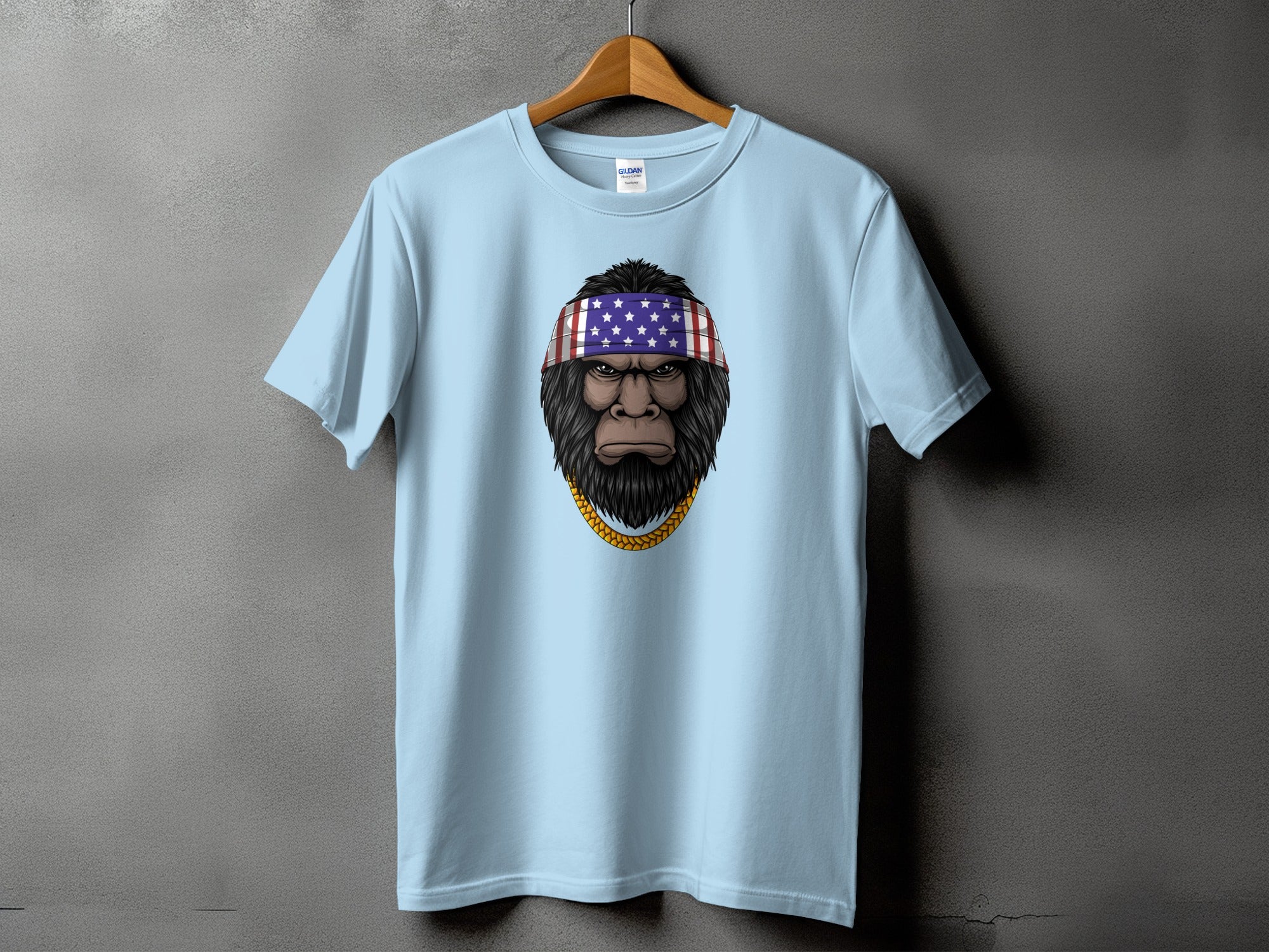 Light blue t-shirt with a Bigfoot graphic wearing an American flag bandana and gold chain.