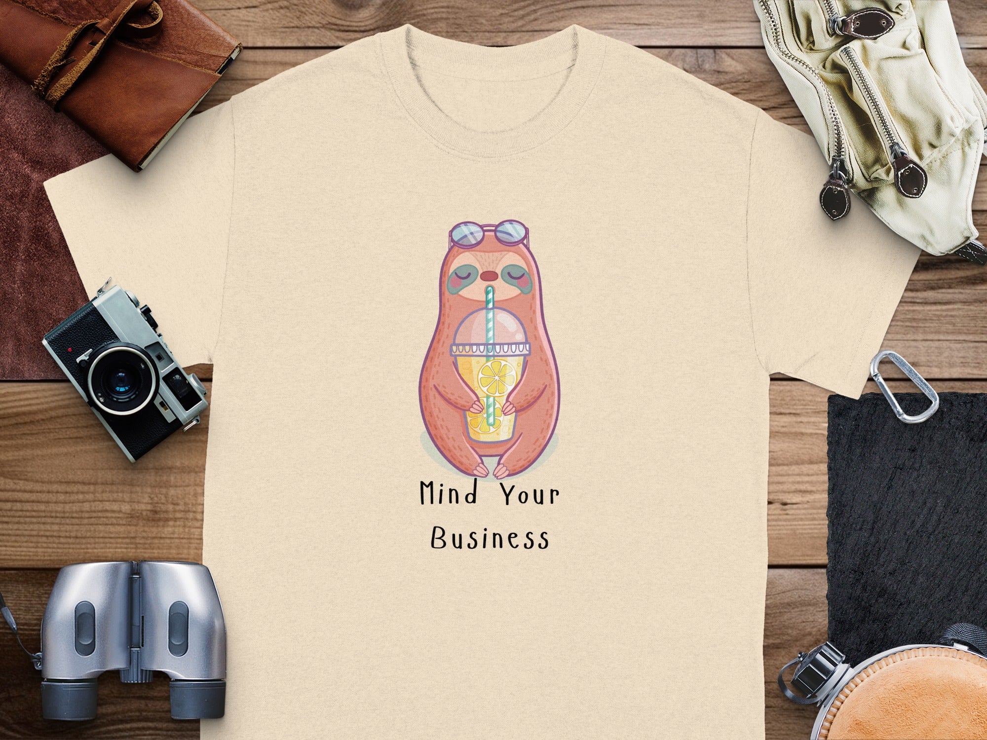 Cream t-shirt with a cartoon sloth drinking from a cup, text "Mind Your Business."
