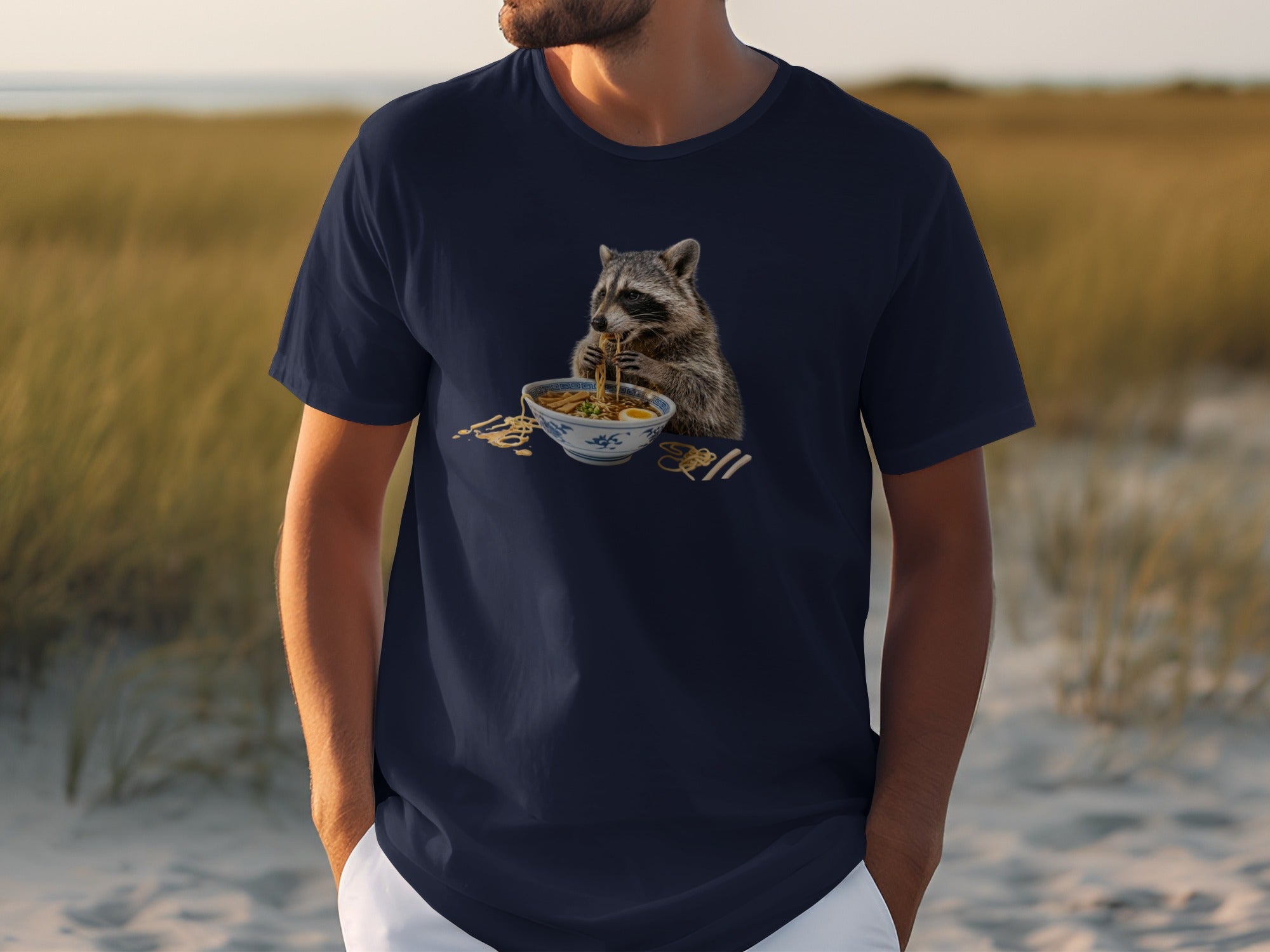 Raccoon eating ramen noodles from a bowl, printed on a navy t-shirt.