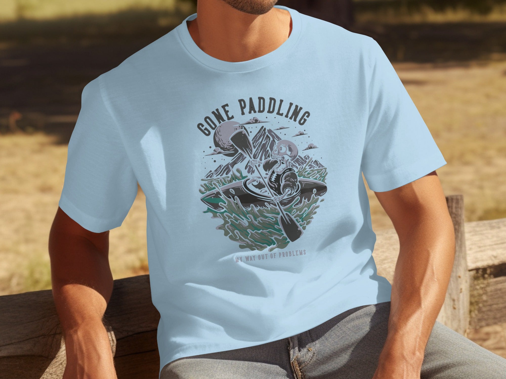 Light blue t-shirt with a graphic of a skeleton in a kayak with text "Gone Paddling" and "My way out of problems."
