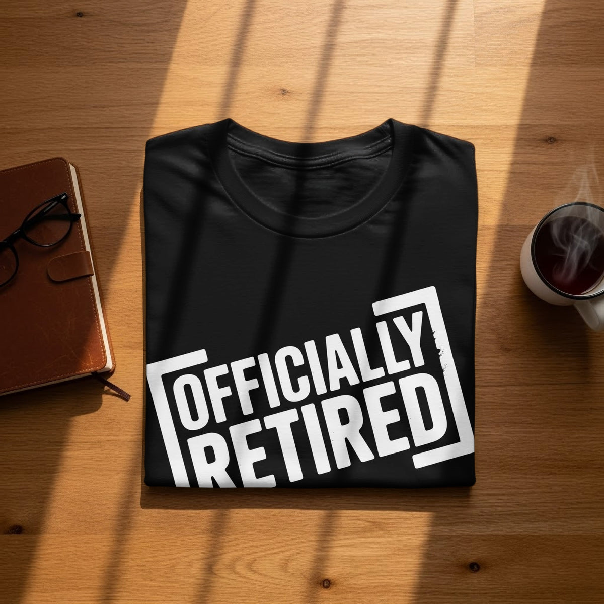 Black t-shirt with "OFFICIALLY RETIRED" graphic, next to a journal and coffee mug.