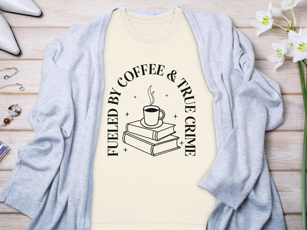 Cream t-shirt with black text "Fueled by Coffee & True Crime" and book illustration.
