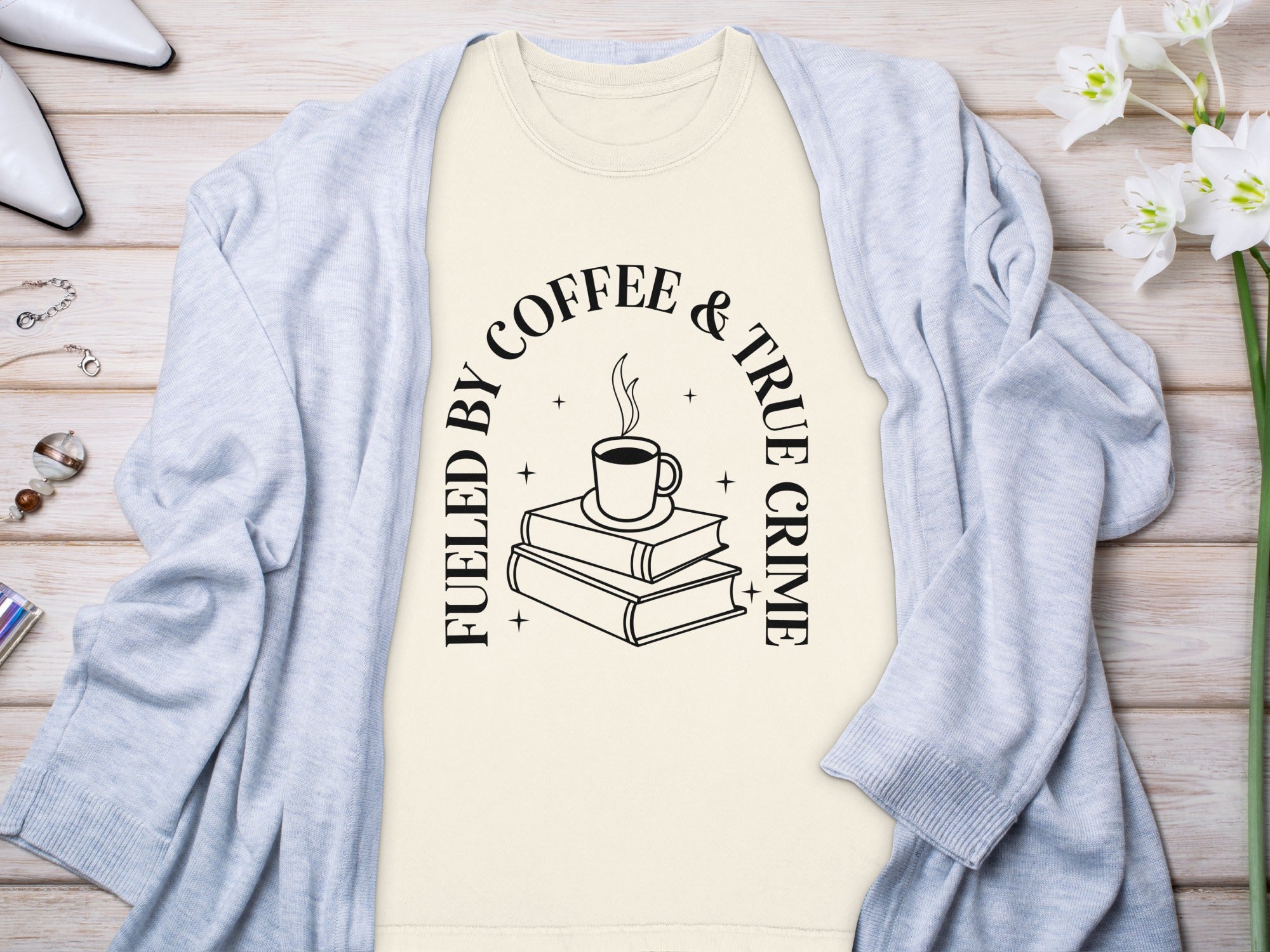 Cream t-shirt with black text "Fueled by Coffee & True Crime" and book illustration.