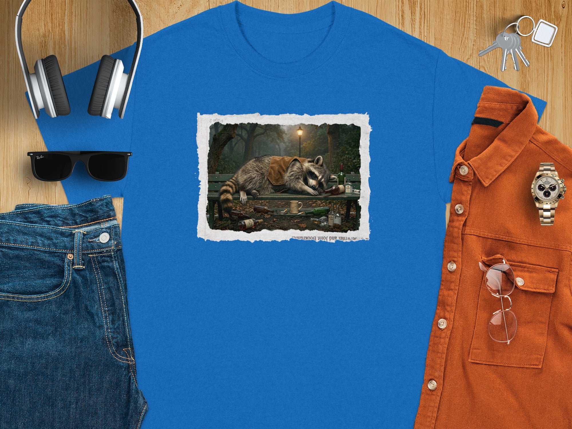 T-shirt with print of sleeping raccoon on park bench with bottles and mug.
