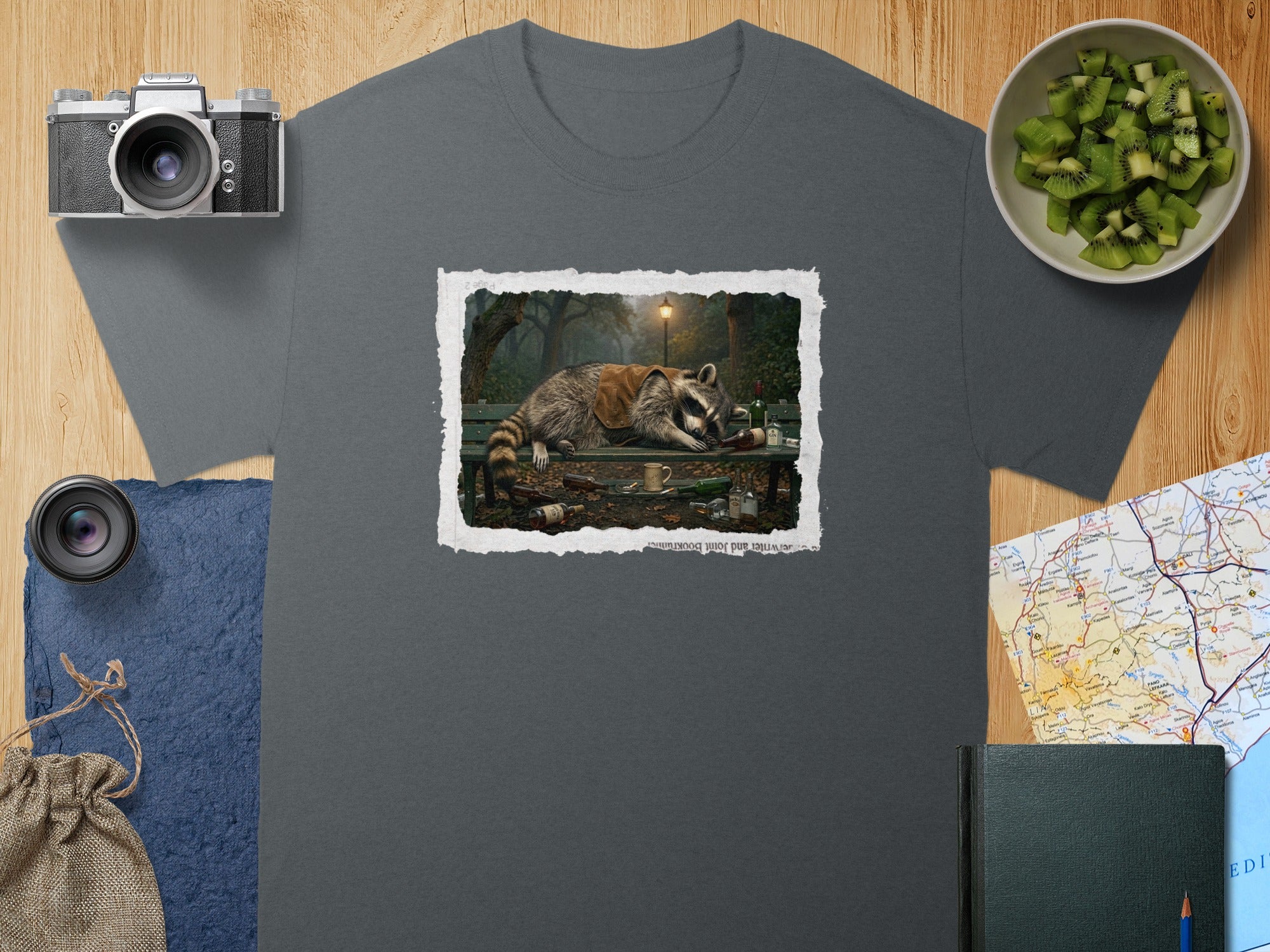 T-shirt with graphic of raccoon sleeping on a bench with bottles.