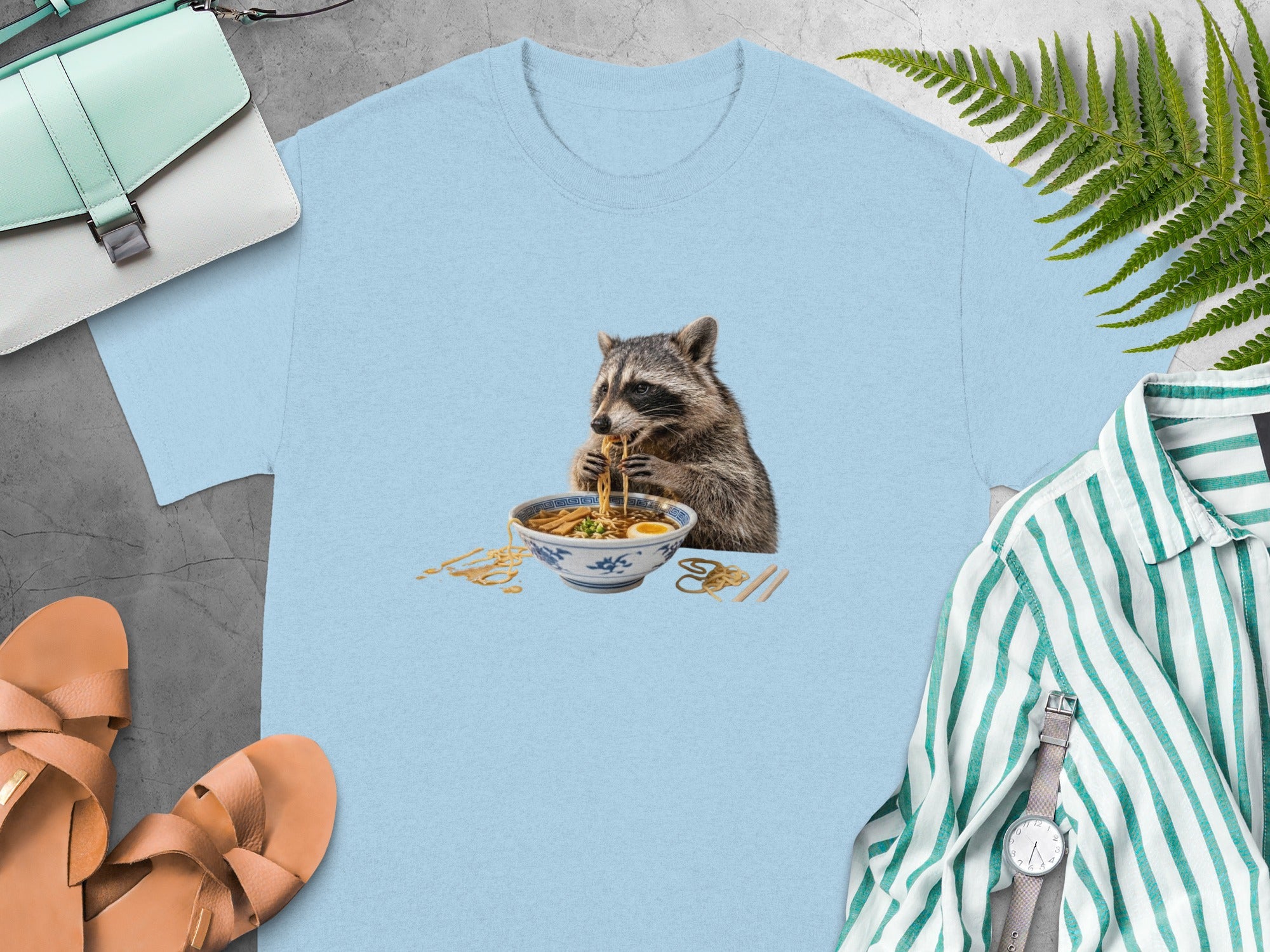 Light blue t-shirt with a raccoon eating ramen noodle soup graphic.