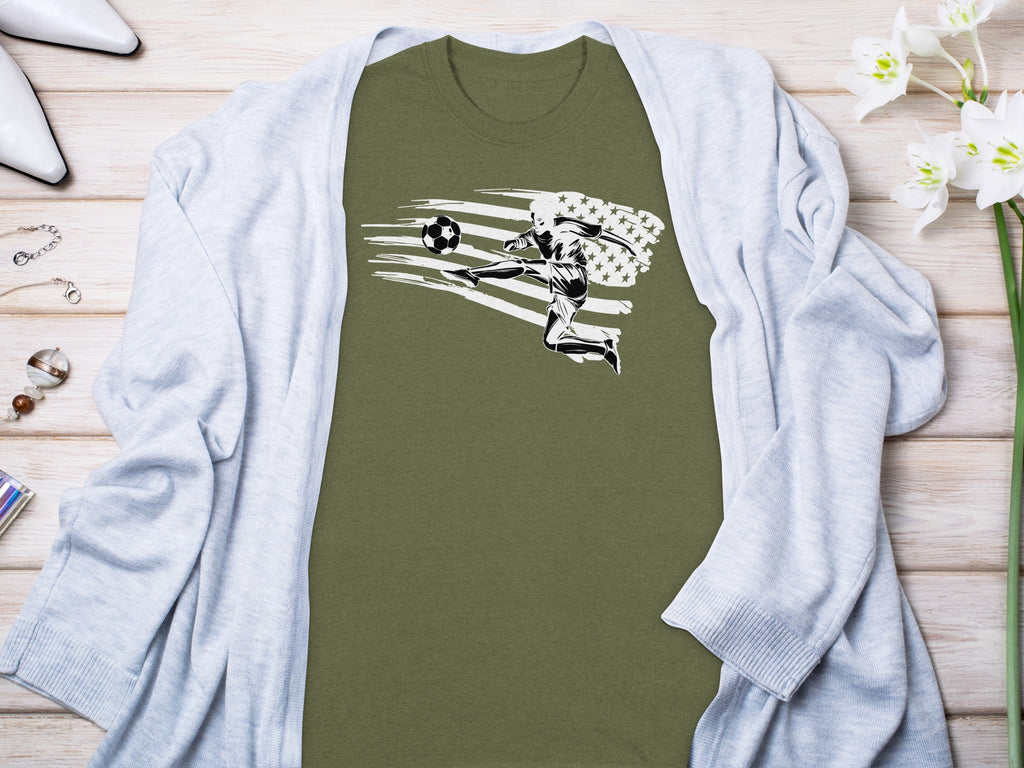 Olive-green t-shirt with a black and white soccer player kicking a ball with an abstract US flag design.