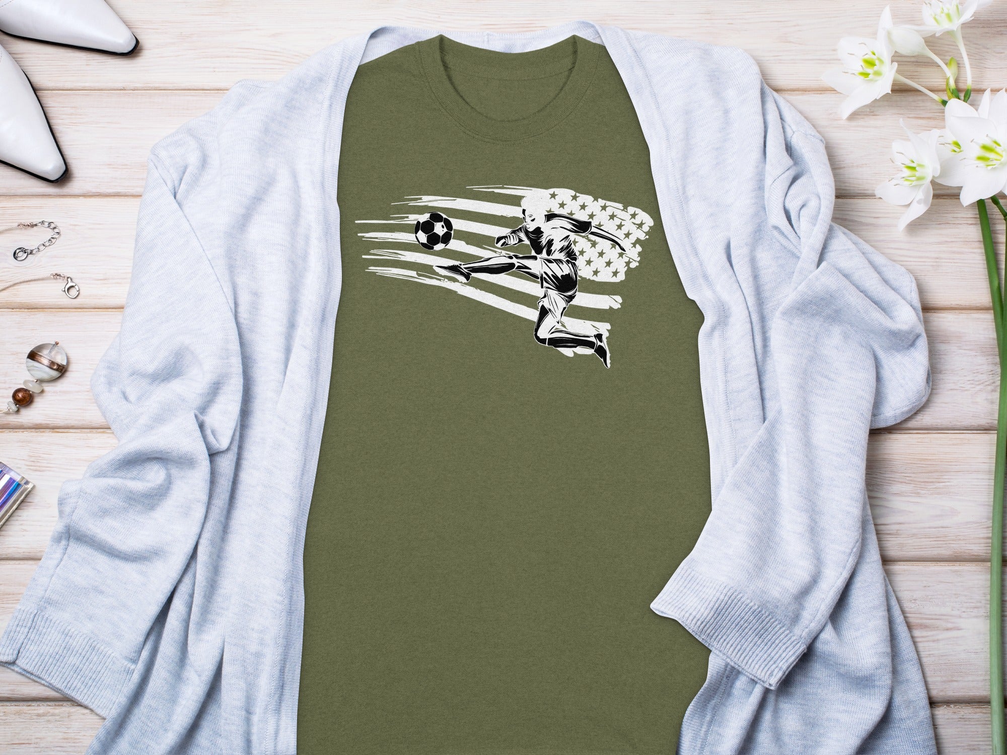 Olive-green t-shirt with a black and white soccer player kicking a ball with an abstract US flag design.