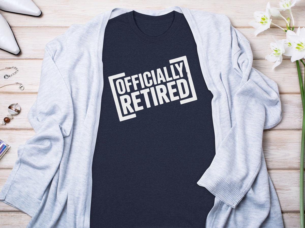 Dark blue t-shirt with white text "OFFICIALLY RETIRED" on a wooden background.