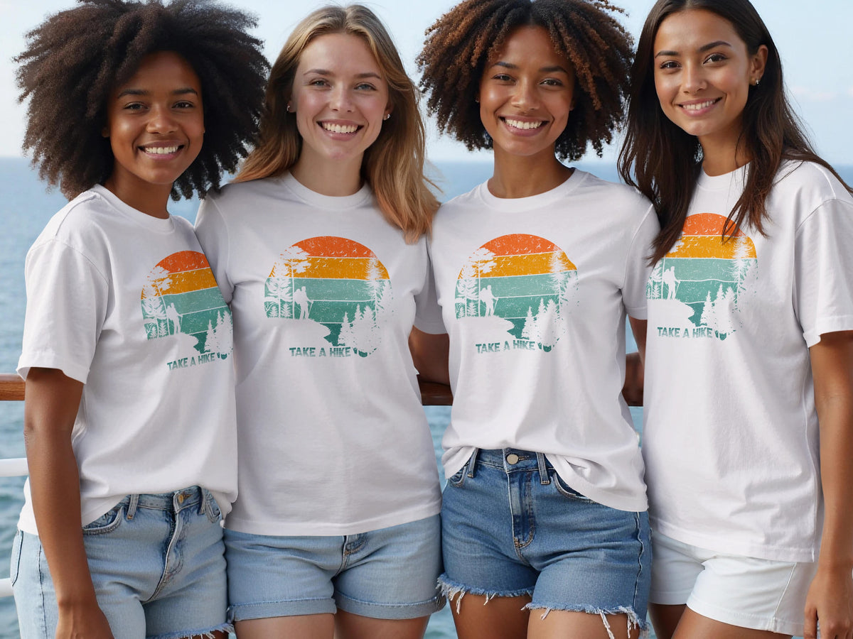 Four smiling women wear white t-shirts with a vintage sunset hike graphic.