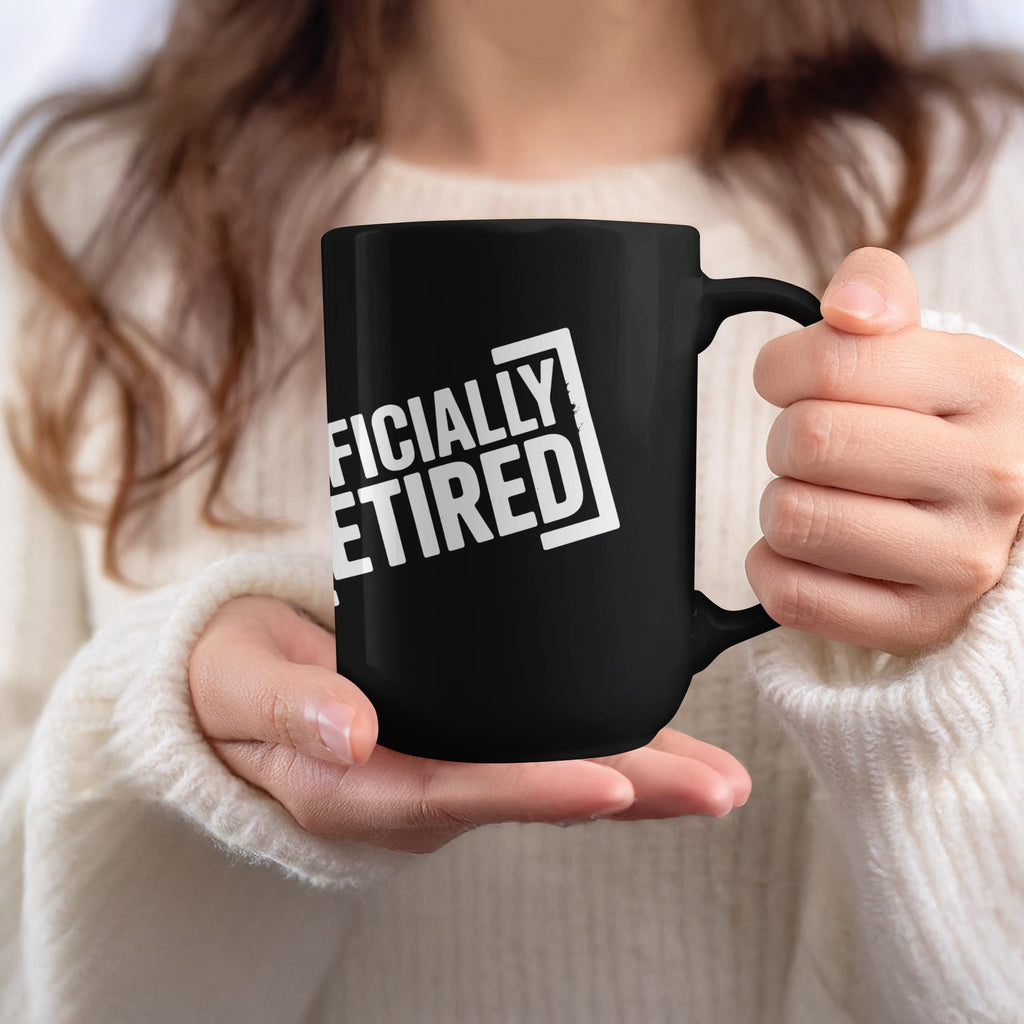 Black mug with white text reading "OFFICIALLY RETIRED" held by a person.