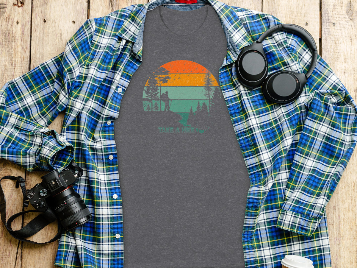 Gray t-shirt with sunset hiker graphic, open plaid shirt, headphones, and camera.
