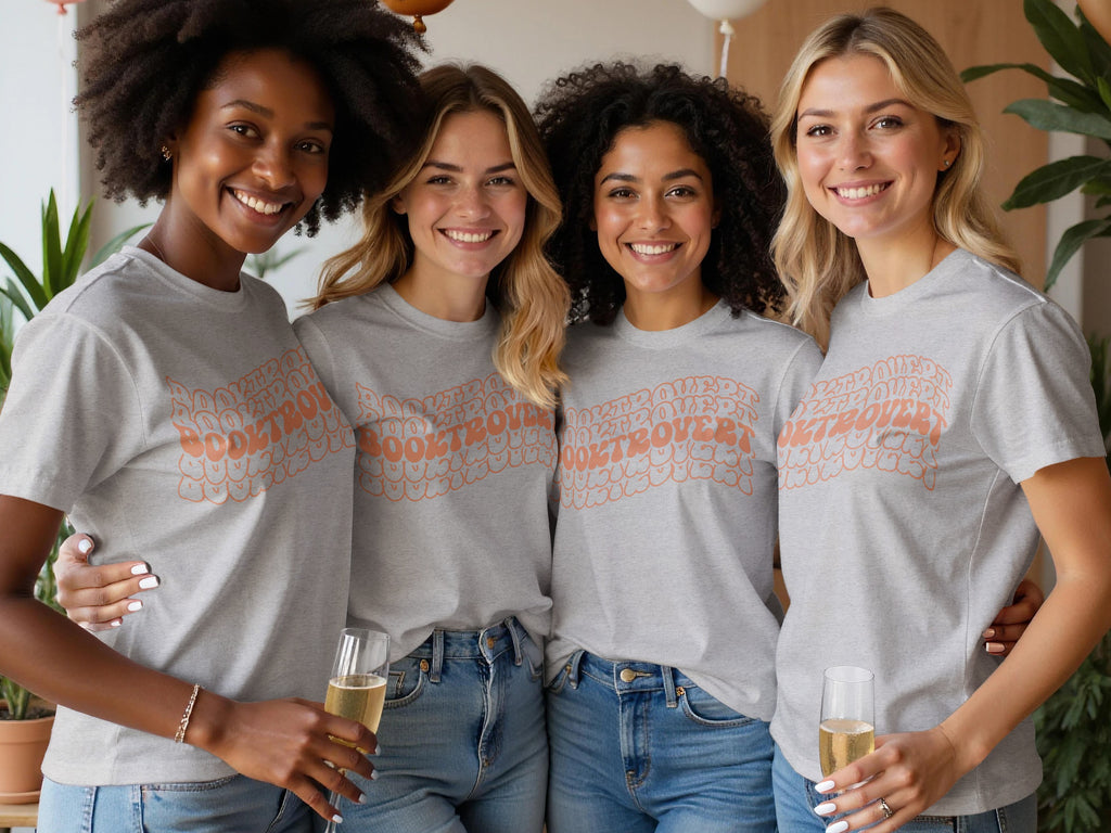 Four women in grey t-shirts with "Booktrovert" text and holding champagne.