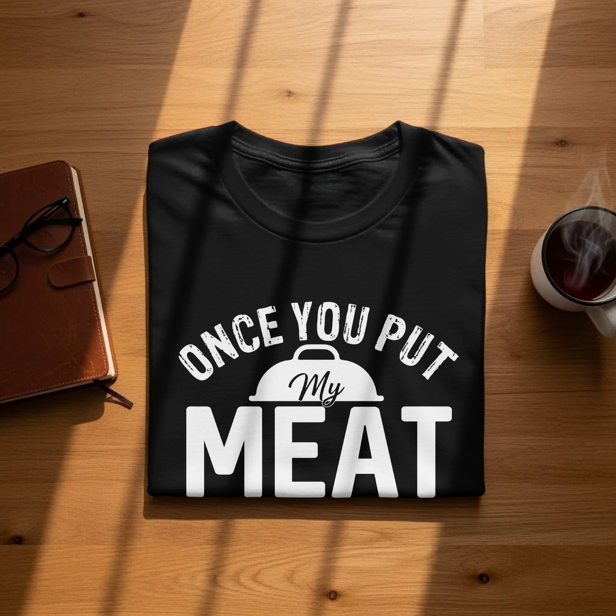 Black t-shirt with "Once You Put My Meat" graphic on a wooden surface.