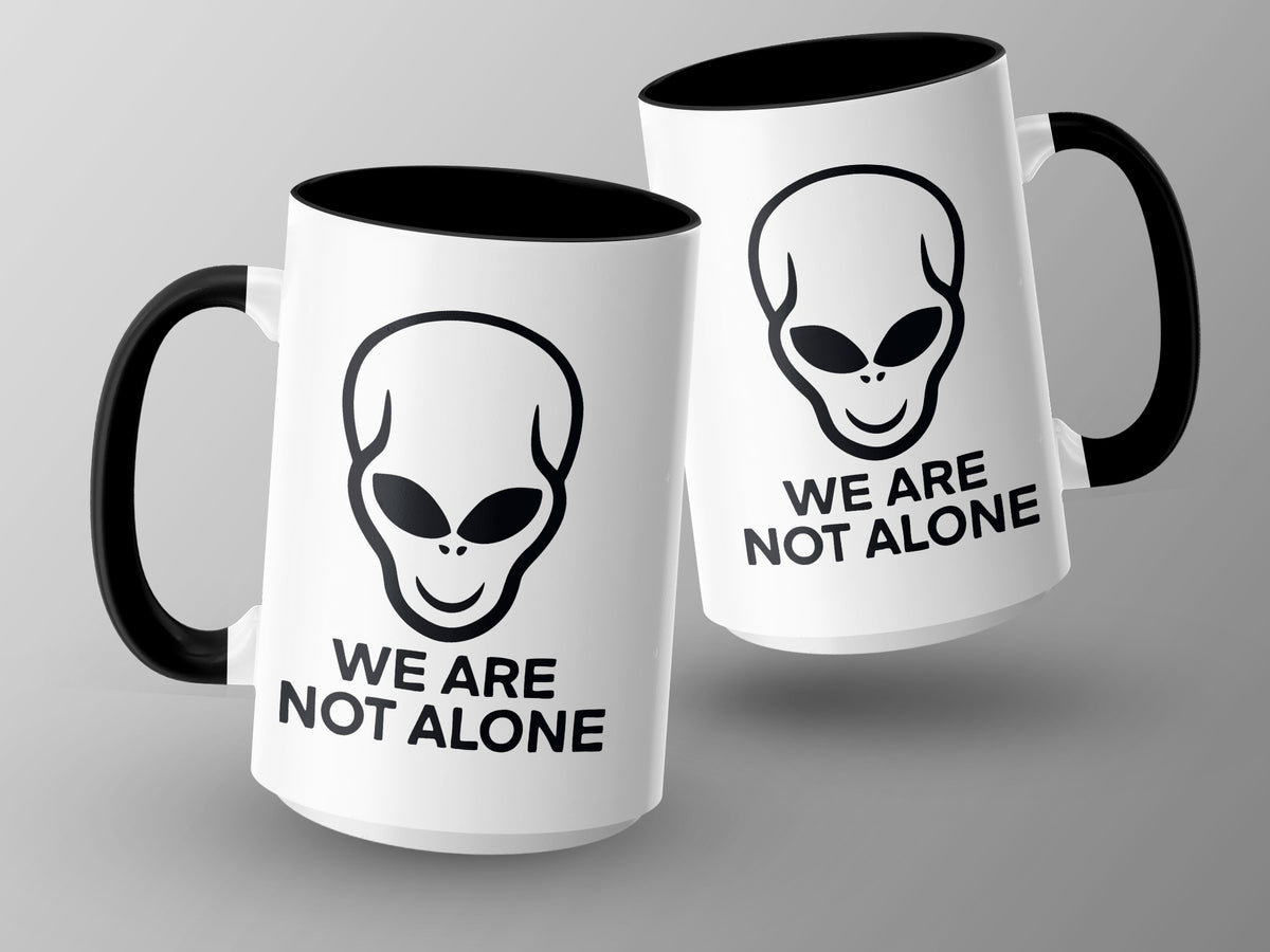 Two white mugs with black handles and rims, featuring alien faces and text.