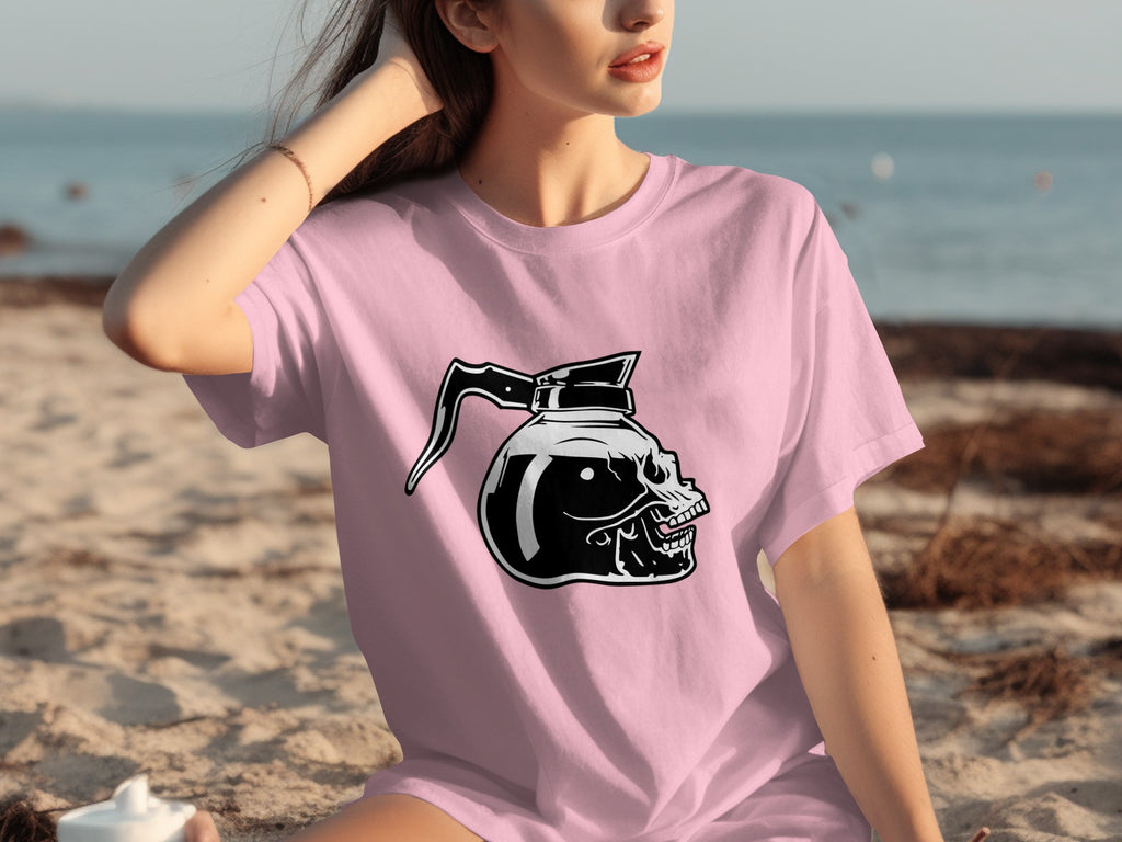 Pink t-shirt with a black graphic of a skull-shaped coffee pot on the beach.