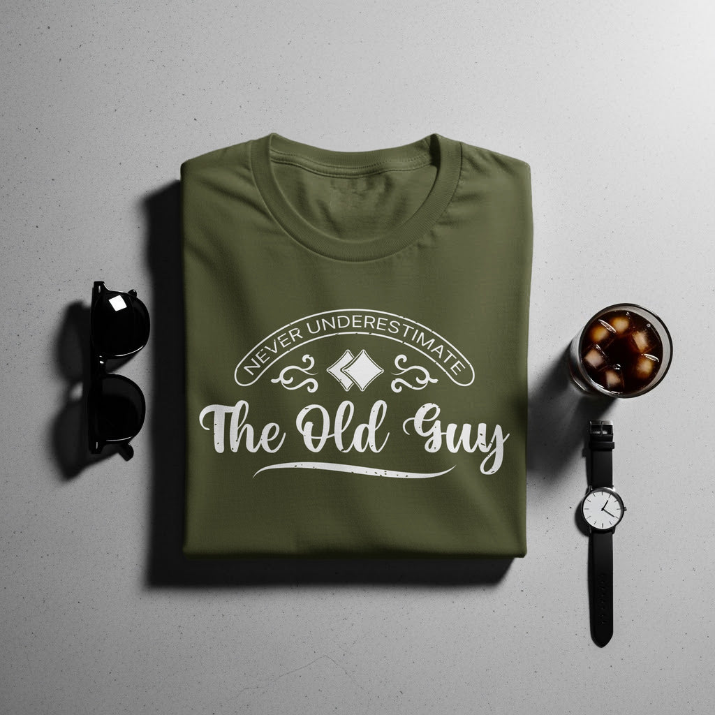 Olive green t-shirt with white text that reads "Never Underestimate The Old Guy".