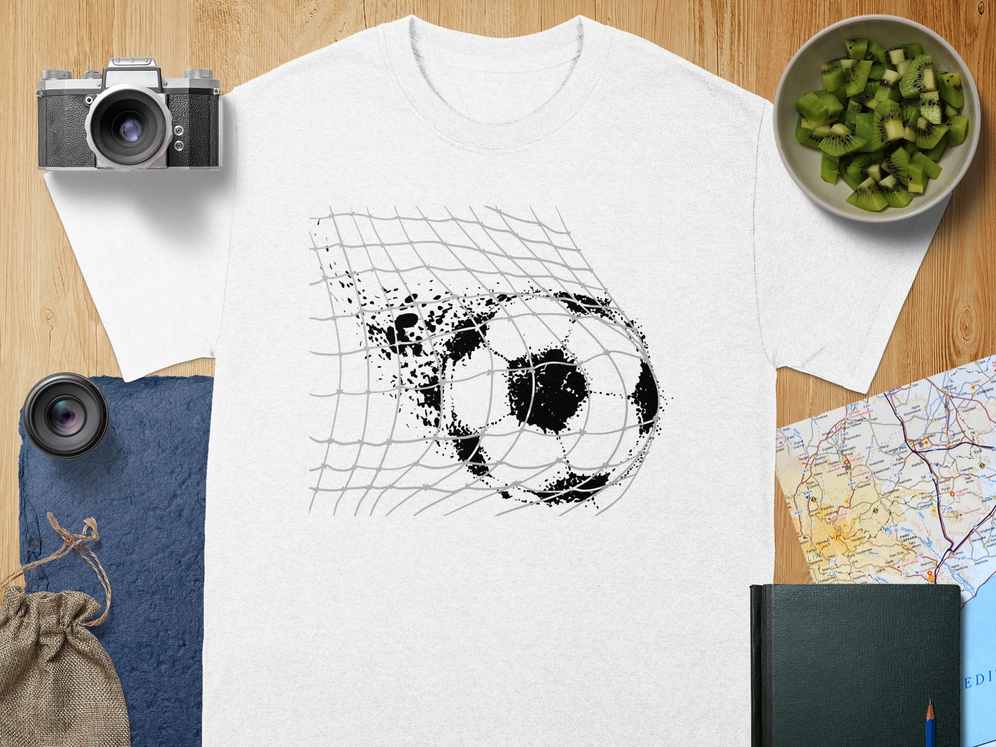 White t-shirt with a gritty black soccer ball breaking through a net graphic.