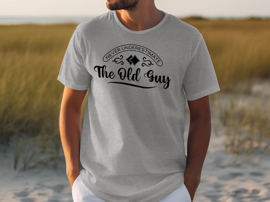 Grey t-shirt with black text "Never Underestimate The Old Guy" on chest.