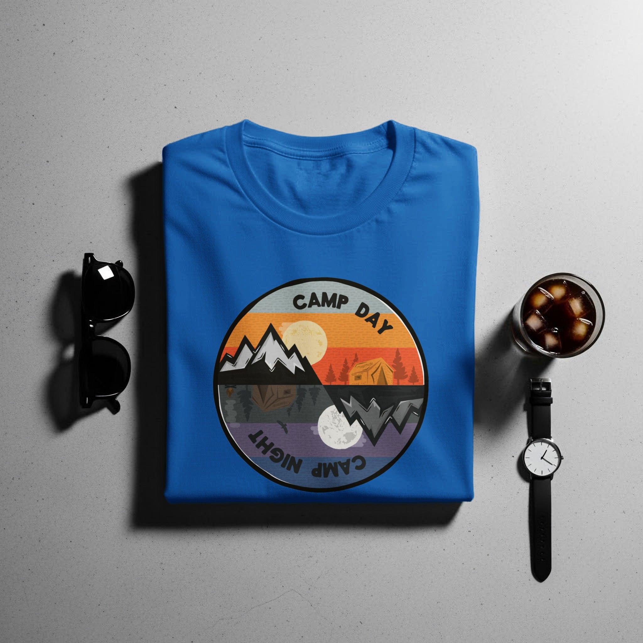 Blue t-shirt with a circular graphic showing mountains, a tent, sun, and moon with "CAMP DAY" and "CAMP NIGHT" text.