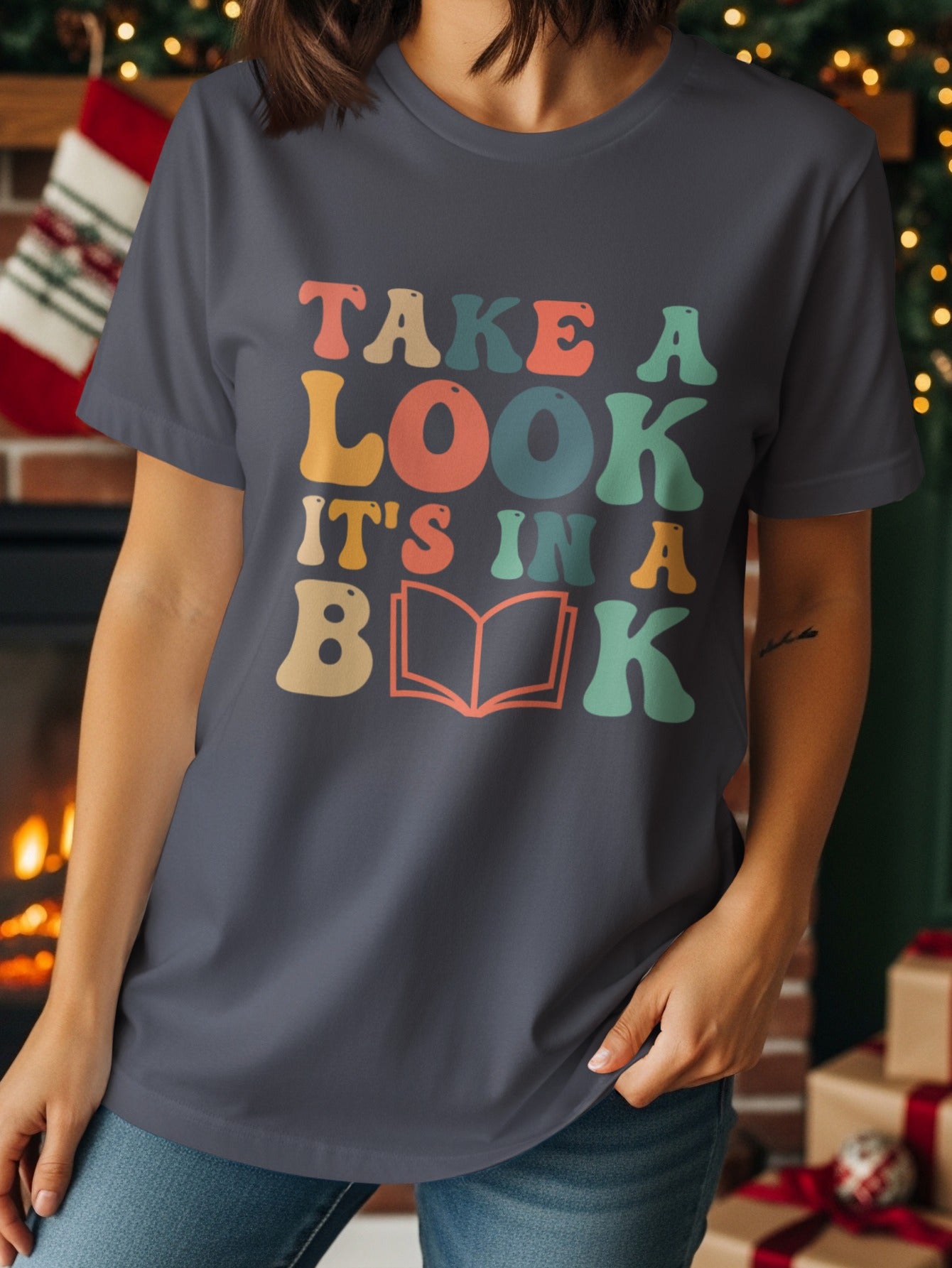 Dark grey t-shirt with colorful text reading "TAKE A LOOK IT'S IN A BOOK" and an open book graphic.